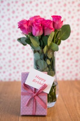 bunch-pink-roses-vase-with-pink-gift-leaning-against-it-happy-birthday-card_13339-49169(1)