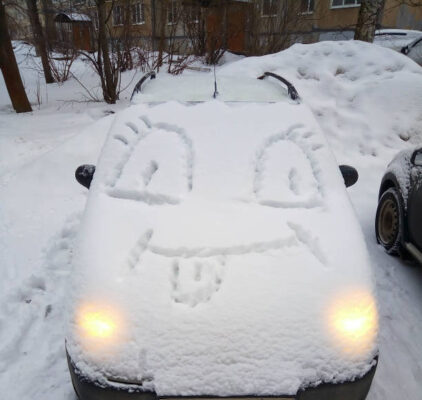A car covered in snow, with a funny face on the hood. Winter fun.